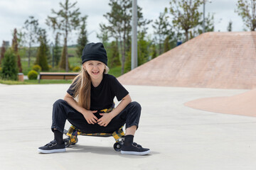 Pretty happy little girl riding on skateboard in skate park in summer day