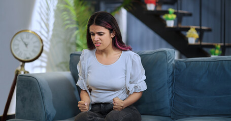 Indian Asian Hindu gen z lonely young girl female burst of anger feel bad hurtful upset sitting alone sofa couch indoor home tired tensed sad angry woman tension lost job regret mistake room house - obrazy, fototapety, plakaty