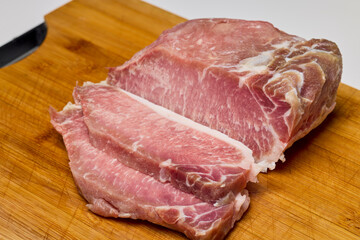 Pork on a wooden chopper cut into pieces to be cooked.
