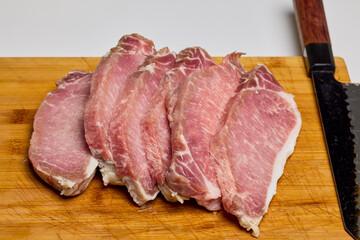 Pork on a wooden chopper cut into pieces to be cooked.