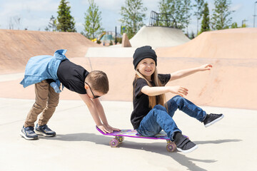 Portrait of stylish siblings children boy and girl in the skate park with skates. Children have fun outdoor in the park