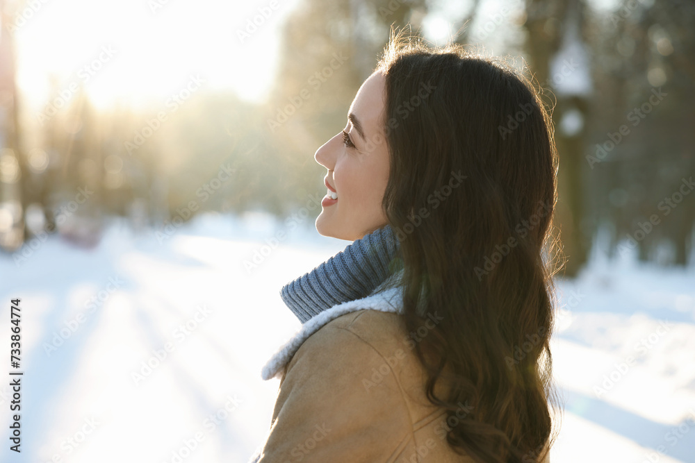 Wall mural Portrait of smiling woman in sunny snowy park. Space for text