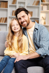 Joyful family moment captured at home: smiling father and his young daughter hugging on plush couch