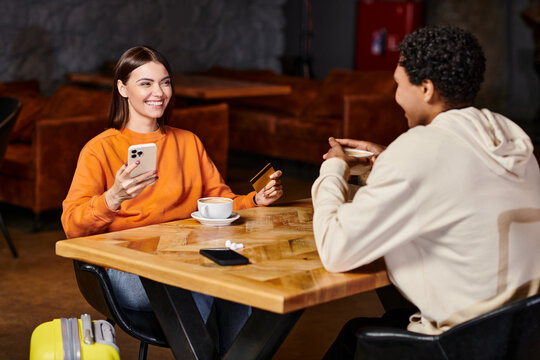 diverse couple sharing quiet conversation at table, woman holding smartphone and credit card