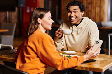 cheerful black man looking at woman sit at a wooden table with smartphone in local cafe, lunch time