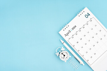 April 2024, Monthly desk calendar for 2024 year and alarm clock with paper clips on blue color...