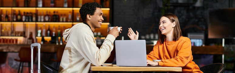 black man and woman laughing and talking at a cafe table, with their laptop beside them, banner - obrazy, fototapety, plakaty
