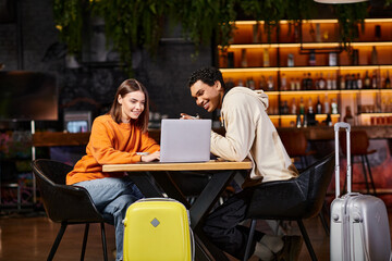 Fototapeta premium black man and woman looking at laptop on cafe table, with their luggage beside them, travel