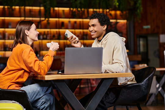 happy diverse couple using a laptop and smartphone in a modern cafe setting for work or study