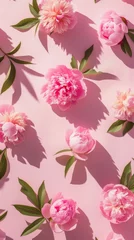 Plexiglas foto achterwand Vivid pink peonies with lush green leaves scattered on a bright pink surface, casting soft shadows in sunlight © Glittering Humanity