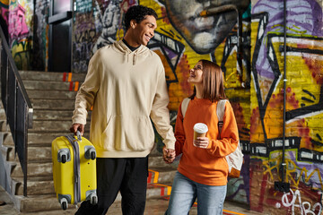 diverse couple holding hands and smiling with a yellow suitcase in a graffiti-painted wall, hostel