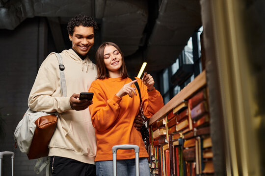 Cheerful couple with smartphone enjoying their time in hostel with library, looking at credit card