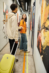 Fototapeta na wymiar Young multicultural couple smiling and walking with suitcases in a modern hostel hallway