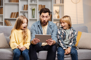 Father and his two kids look on tablet screen. Funny shock has them all with mouths open