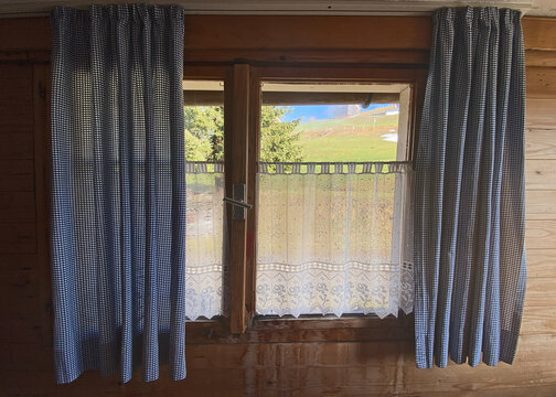 Bergh&uuml;tte, Holzfenster, wei&szlig;e gekl&ouml;ppelt Gardienen als Sichtschutz am Fenster befestigt, daneben auf beiden Seiten blaugraue Gardinen