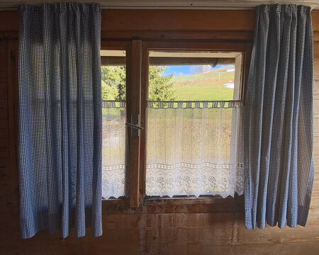 Skih&uuml;tte, Holzfenster, wei&szlig;e gekl&ouml;ppelt Gardienen als Sichtschutz am Fenster befestigt, daneben auf beiden Seiten blaugraue Gardinen