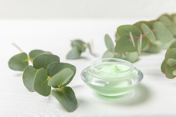 Jar of moisturizing cosmetic cream for face, hands and body with eucalyptus leaves on a white wooden background. Natural organic product. Beauty and spa concept. Body care. Space for text.Copy space.