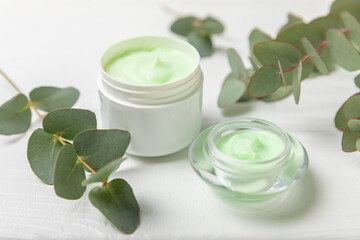 Fototapeta na wymiar Jar of moisturizing cosmetic cream for face, hands and body with eucalyptus leaves on a white wooden background. Natural organic product. Beauty and spa concept. Body care. Space for text.Copy space.
