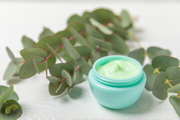 Obraz na płótnie Canvas Jar of moisturizing cosmetic cream for face, hands and body with eucalyptus leaves on a white wooden background. Natural organic product. Beauty and spa concept. Body care. Space for text.Copy space.