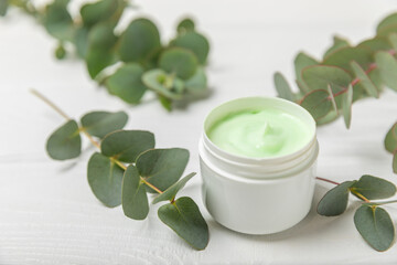 Jar of moisturizing cosmetic cream for face, hands and body with eucalyptus leaves on a white wooden background. Natural organic product. Beauty and spa concept. Body care. Space for text.Copy space.