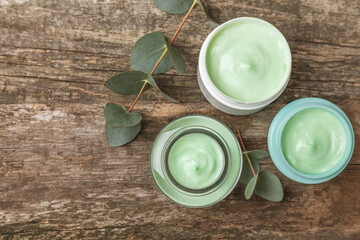 Jar of moisturizing cosmetic cream for face, hands and body with eucalyptus leaves on brown wooden background. Natural organic product. Beauty and spa concept. Body care. Space for text.Copy space.