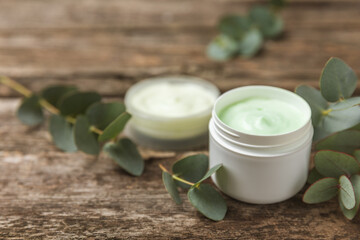 Jar of moisturizing cosmetic cream for face, hands and body with eucalyptus leaves on brown wooden background. Natural organic product. Beauty and spa concept. Body care. Space for text.Copy space.