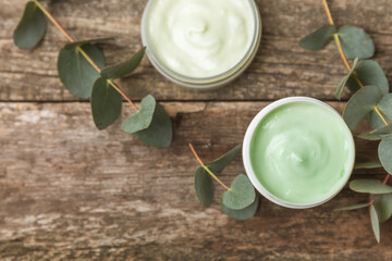 Jar of moisturizing cosmetic cream for face, hands and body with eucalyptus leaves on brown wooden background. Natural organic product. Beauty and spa concept. Body care. Space for text.Copy space.