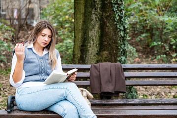 Young businesswoman taking a break from work sitting in the park relaxing while reading a book. Business female office worker read outdoor during lunch break to clear her mind for new job opportunity