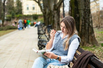 Young businesswoman taking a break from work sitting in the park relaxing while reading a book....
