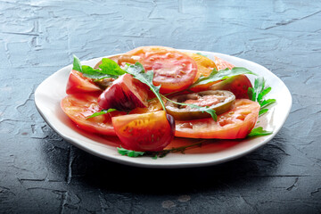 Fresh tomato and rocket salad. A variety of tomatoes of different sorts with arugula leaves. Healthy summer food on a black slate background