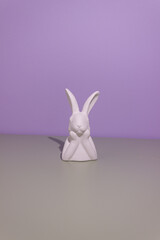 White easter bunny propping up its snout with its paws on a purple grey background.