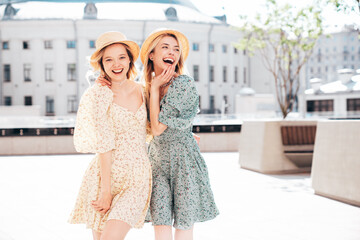 Two young beautiful smiling hipster female in trendy summer dress  clothes. Blond carefree women posing in the street. Positive models having fun at sunny day. Going crazy. In sundress