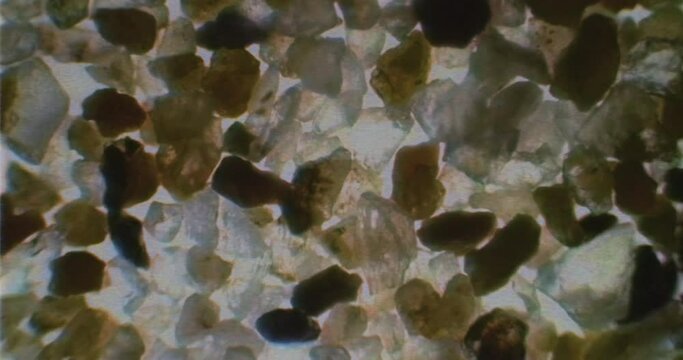 VHS videotape of sand sample under a microscope with floating bacteria and germs. Old-school recording of crystal rocks under a microscope lens. Microscopic world.