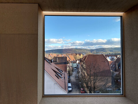 Quadratisches Fenster ge&ouml;ffnet mit Blick auf D&auml;cher und blauer Himmel