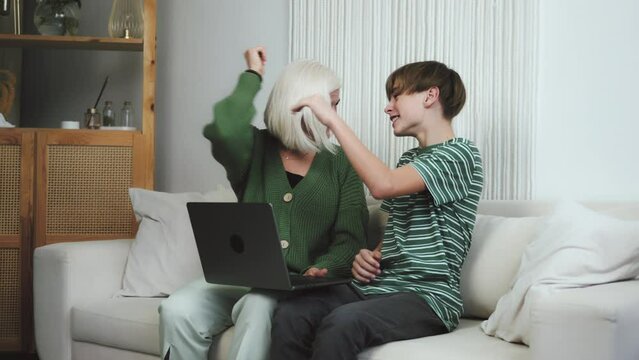 Happy Granny and boy grandson using laptop computer and giving five each other, successful shopping. Family Doing homework, typing messages, scrolling, browsing internet together. Two generations