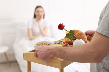 Romantic breakfast. Husband bringing tray with tasty food to his wife in bedroom, closeup. Space...