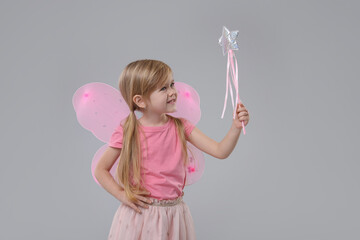 Cute little girl in fairy costume with pink wings and magic wand on light grey background