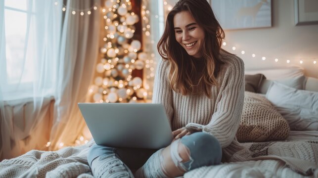 Happy casual beautiful woman working on a laptop sitting on the bed in the house.