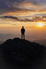Obraz premium Silhouette of a successful businessman, a man in a suit, standing on top of a mountain and looking at the sunrise, on the background of rocks. Created by artificial intelligence.