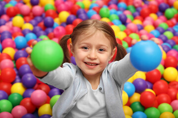 Fototapeta na wymiar Happy little girl holding colorful balls in ball pit