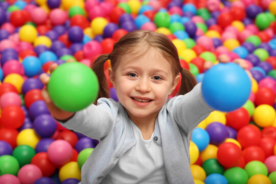 Happy little girl holding colorful balls in ball pit