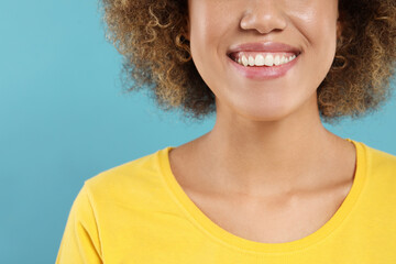 Woman with clean teeth smiling on light blue background, closeup