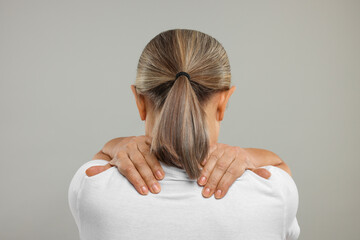 Mature woman suffering from pain in her neck on grey background, back view