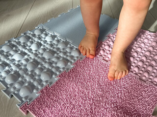 Baby's feet on orthopedic children's massage puzzle mats with colorful parts for the prevention of...