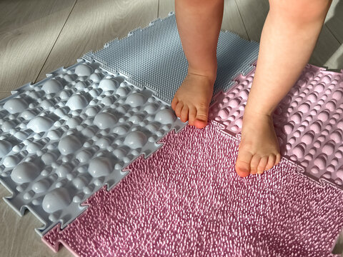 Baby's feet on orthopedic children's massage puzzle mats with colorful parts for the prevention of flat feet, children's health 