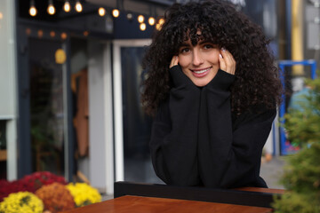 Happy young woman in stylish black sweater at wooden table outdoors, space for text