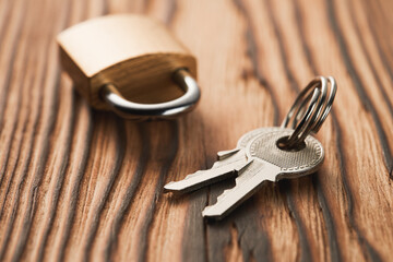 A bunch of keys and a closed padlock in golden color on a wooden background.