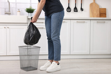 Woman taking garbage bag out of trash bin in kitchen, closeup