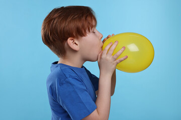 Boy inflating yellow balloon on light blue background