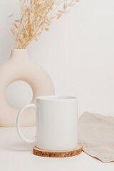 White mockup mug on wooden cup coaster with linen cloth and stylish vase at the background . Mockup mug for logo, branding, print, gift and design. Scandinavian home interior, bohemian style